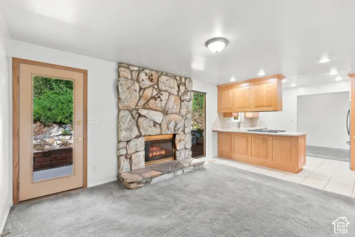 Stone-clad fireplace with hearth, wood-finish cabinetry, light-toned countertop, and recessed lighting