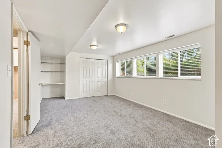 Spacious room with light gray carpeting, multiple windows with blinds, built-in shelving, and a double-door closet