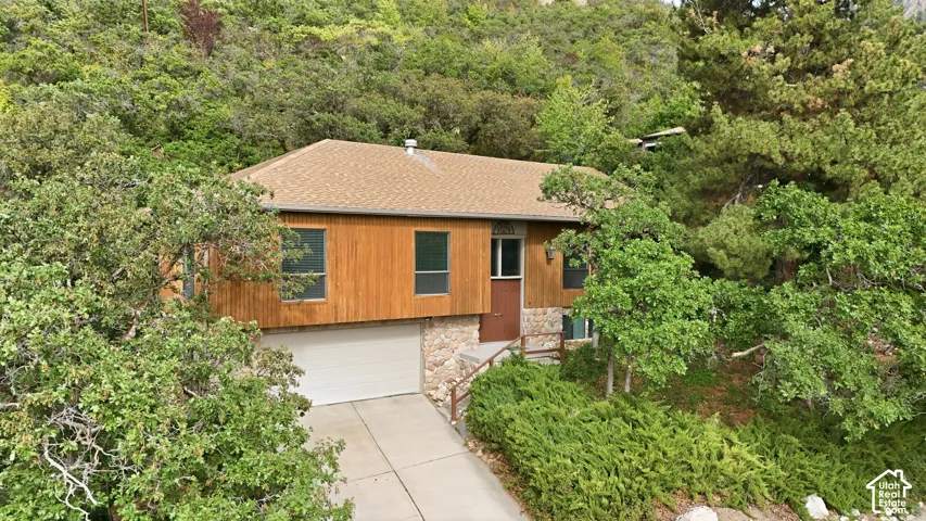 Wood-paneled facade with stone accents, attached garage, and surrounding mature greenery