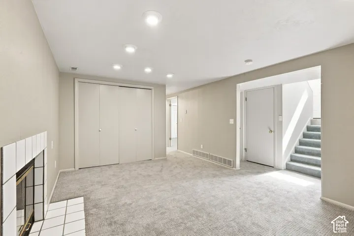 Recessed lighting, light gray carpet, white fireplace with tile surround, white doors, and a staircase with carpeted treads