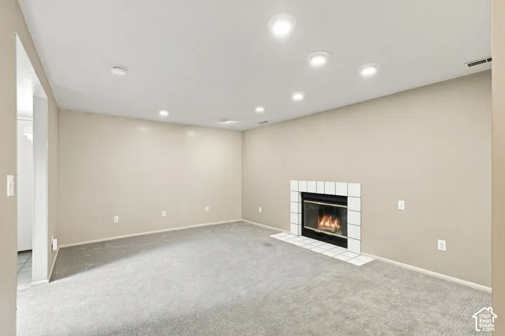 Recessed lighting illuminates a neutral-toned room featuring a central fireplace with a white tile surround and hearth