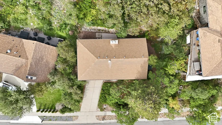 Gabled rooflines with brown shingles, surrounded by mature trees, and a concrete driveway leading to the street