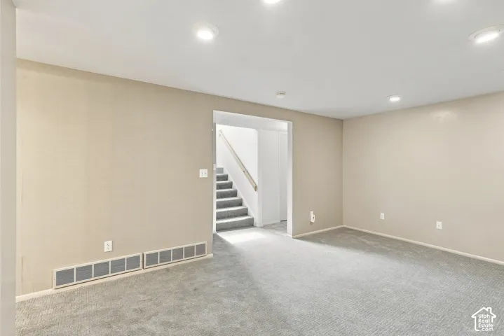 Recessed ceiling lighting, light neutral wall paint, gray carpet flooring, and a stairway with white risers and gray treads