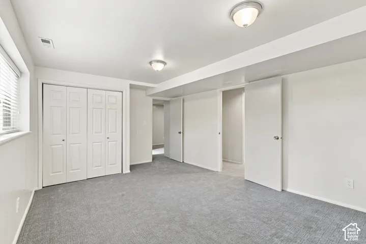 Recessed window with horizontal blinds, grey carpeting, white bi-fold closet doors, white interior doors, and flush mount ceiling lights