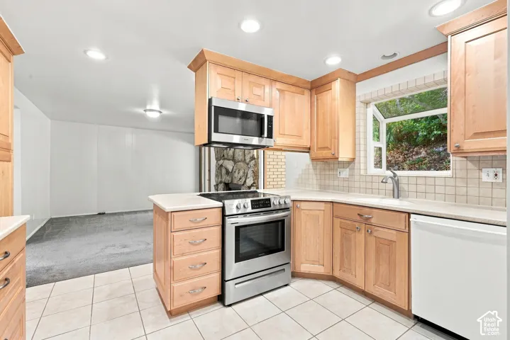 Kitchen featuring wood cabinetry, stainless steel range and microwave, tile backsplash, and light-toned countertops