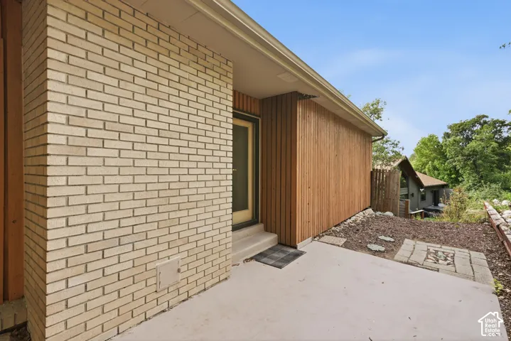 Light-toned brick exterior with vertical wood-panel siding, concrete pathway, and stone accent landscaping