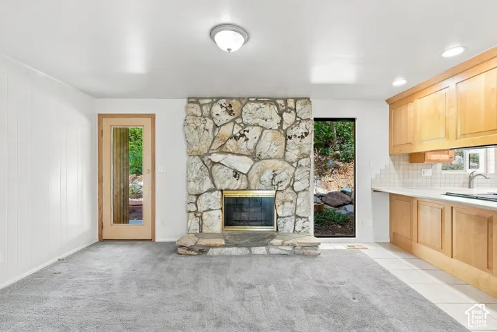 Stone-clad fireplace, kitchen cabinetry with light wood finish, white countertop, tile backsplash, and light wood-frame glass door
