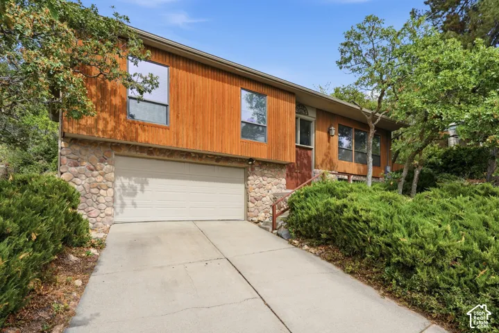 Wood-clad exterior with stone accents, integrated garage, and concrete driveway