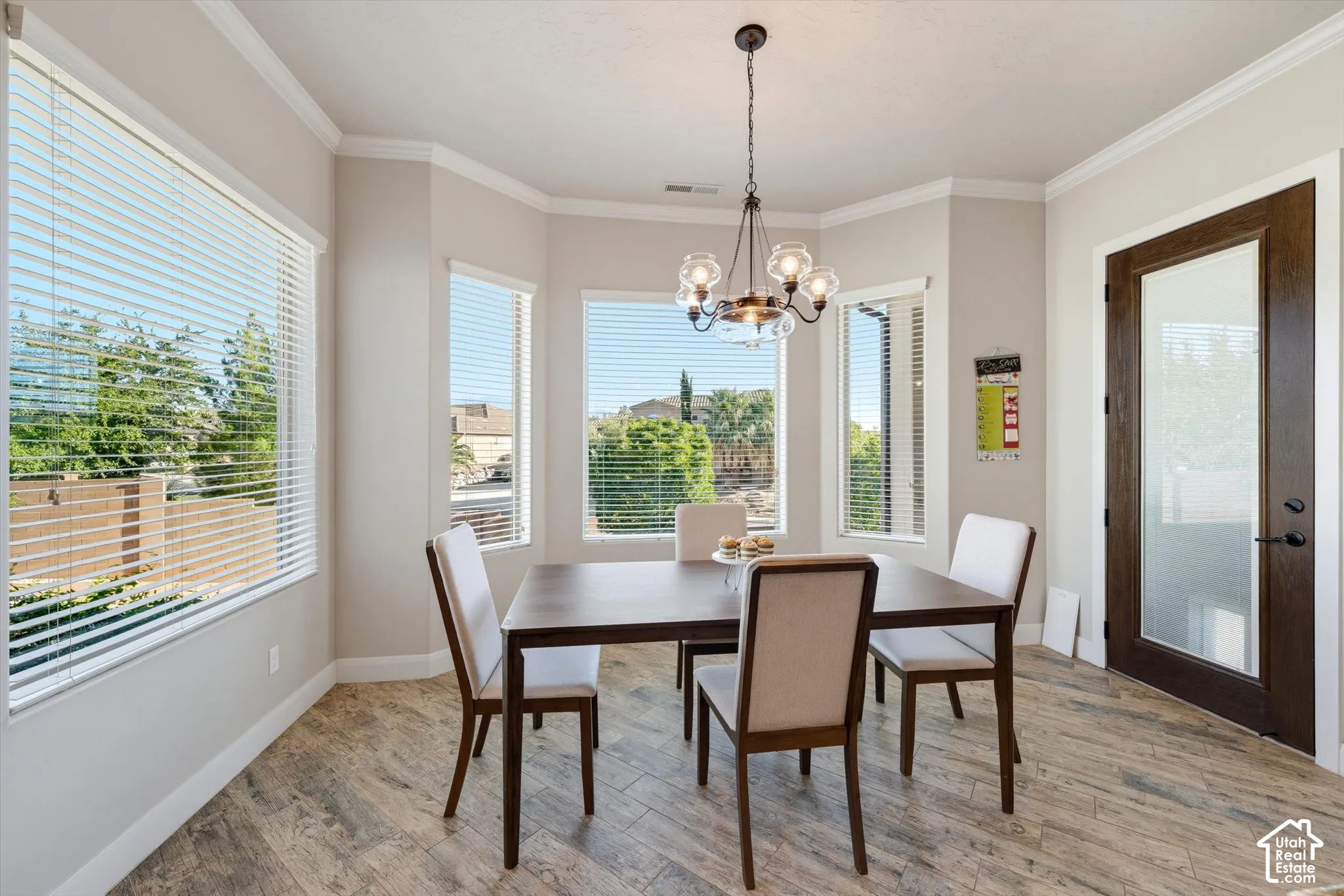 Bay window with multiple large windows, wood-finish flooring, a contemporary chandelier, and a dark wood-paneled door with frosted glass