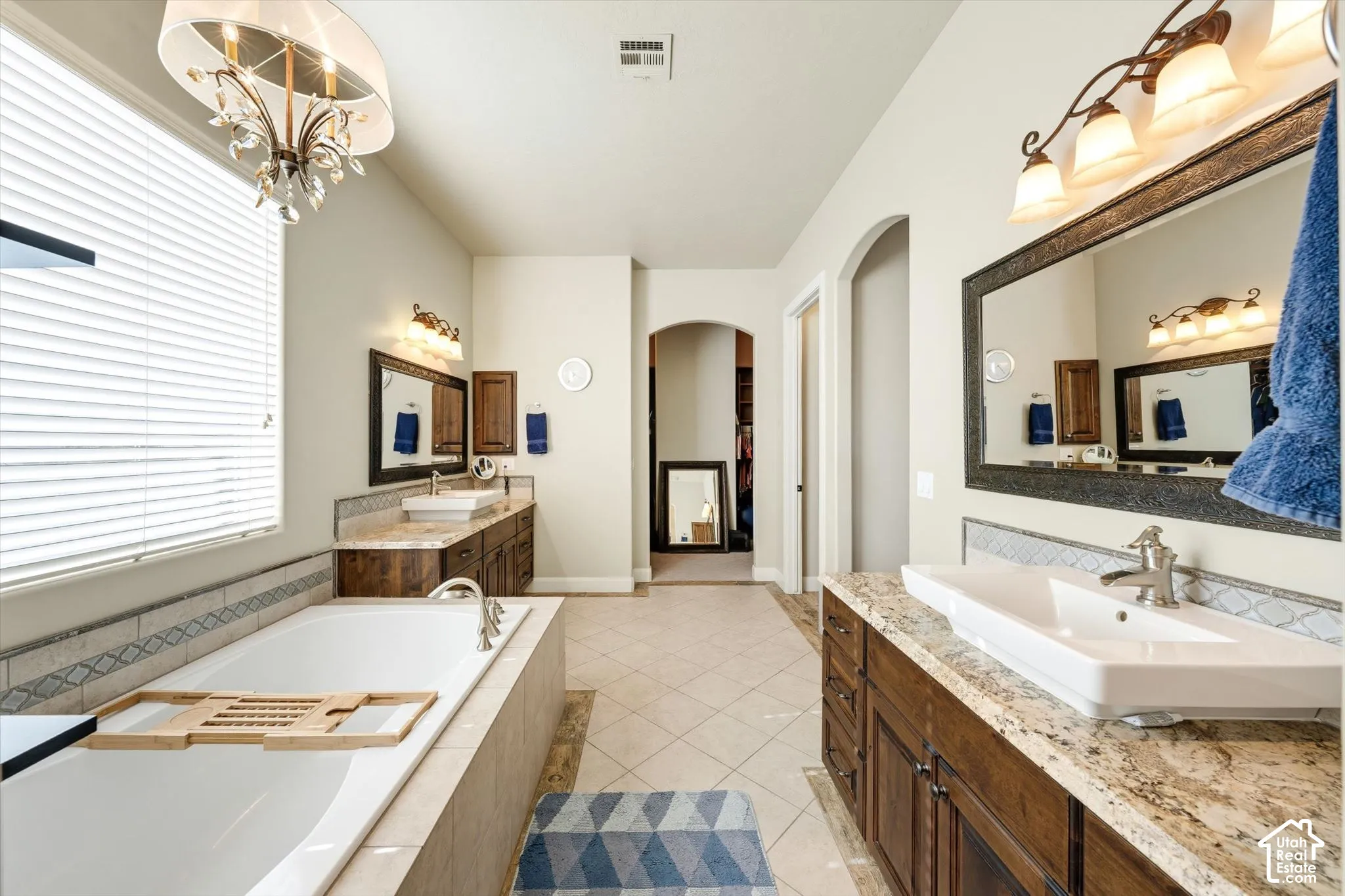 Dual vanities with stone countertops, an expansive soaking tub, and tiled flooring
