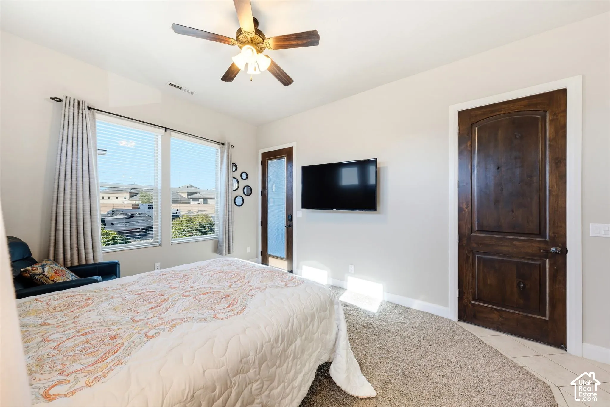 Room featuring expansive windows, a ceiling fan with integrated lighting, a dark wood-paneled door with an arched top, and mixed flooring with carpet and tile