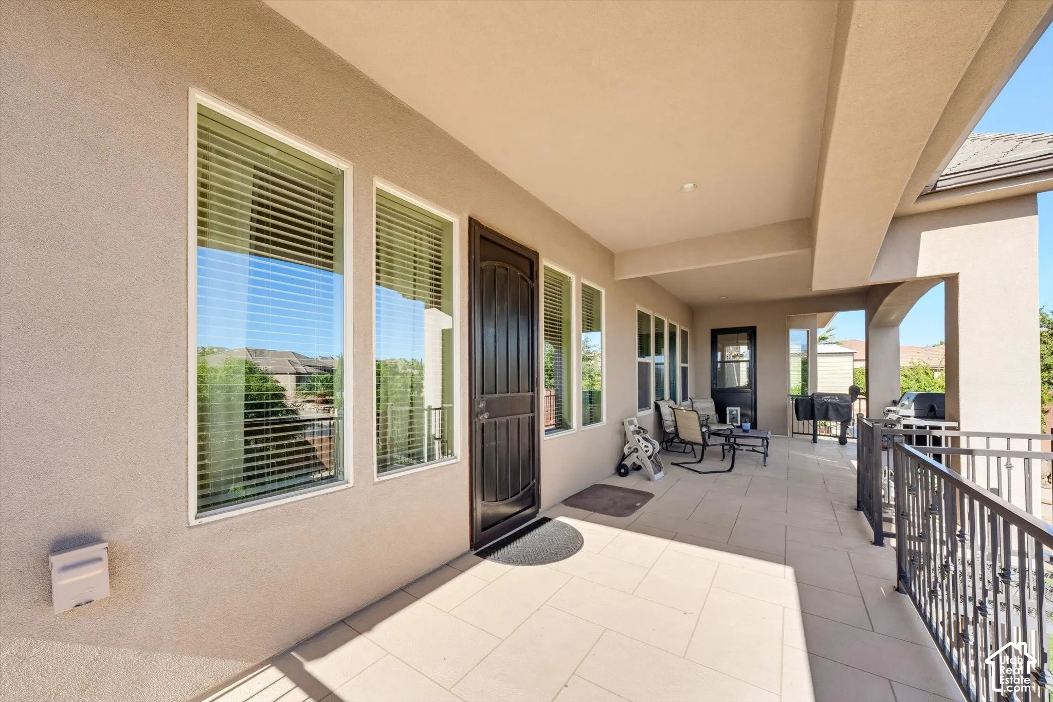 Spacious covered balcony featuring a stucco exterior, tiled flooring, multiple windows, and a black wrought iron railing