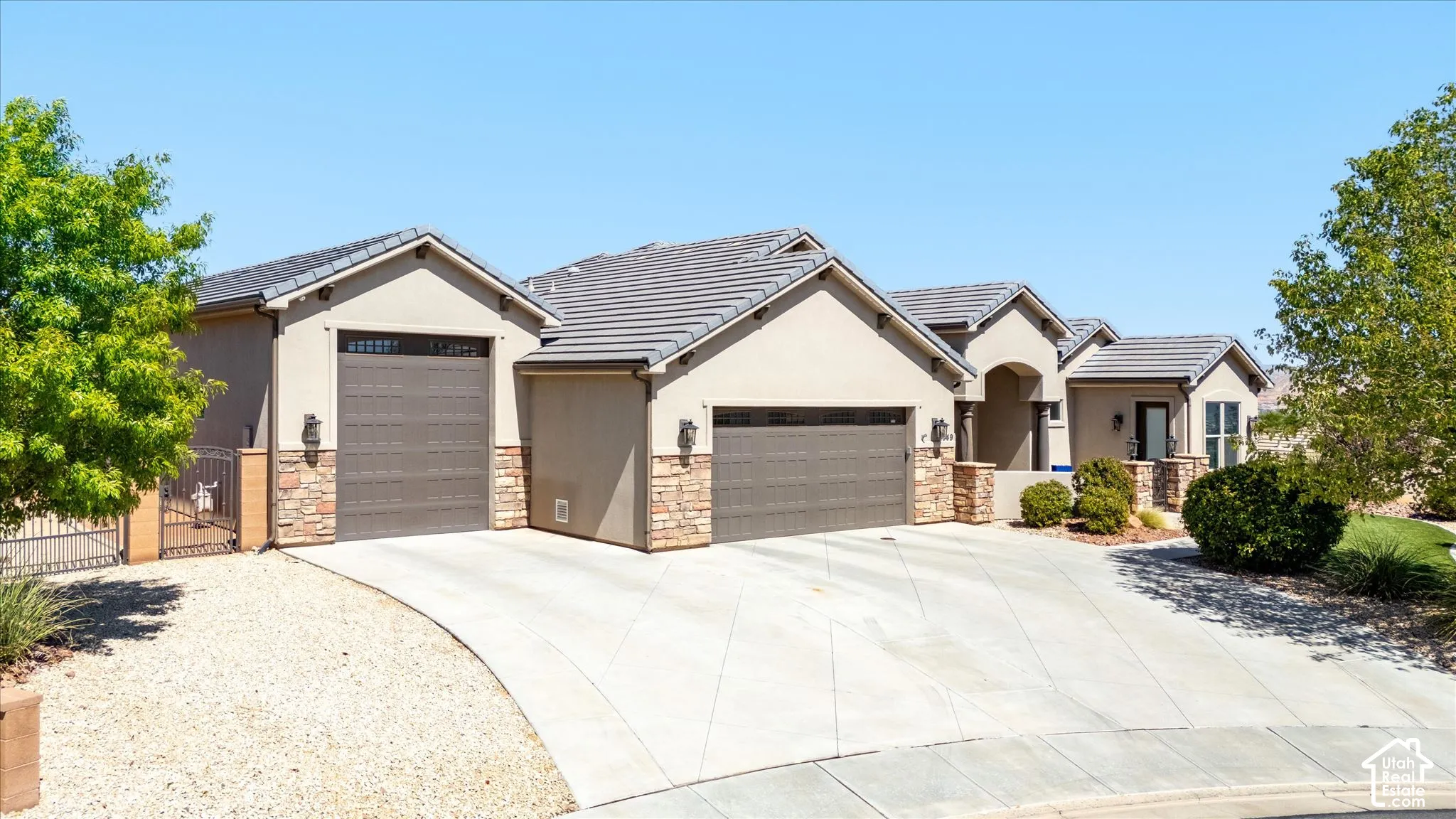 Stucco exterior with stone accents, concrete tile roofing, multiple garage doors, concrete driveway, and established landscaping