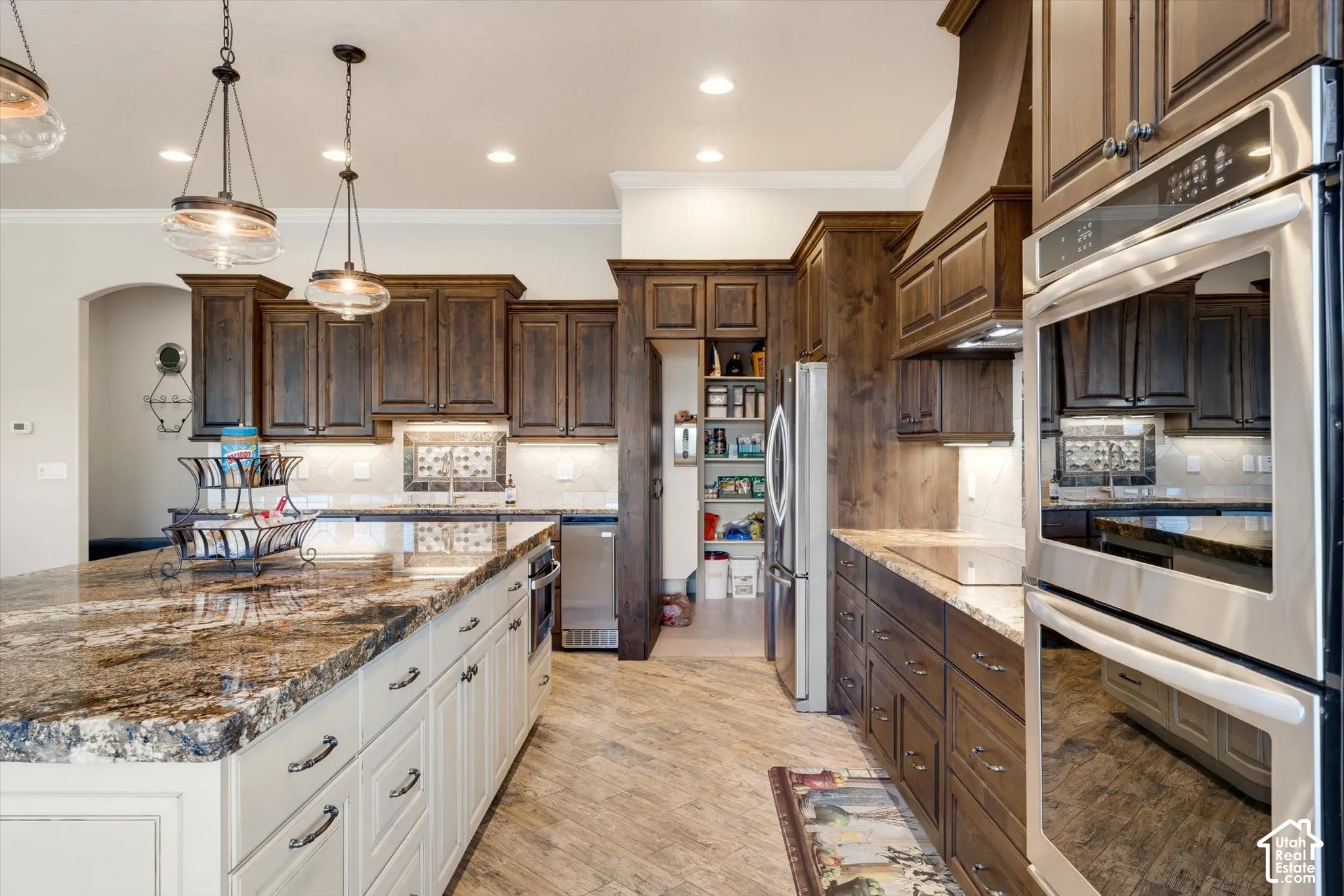 Kitchen featuring an expansive island with a polished stone countertop, rich wood cabinetry, stainless steel double ovens, and recessed lighting