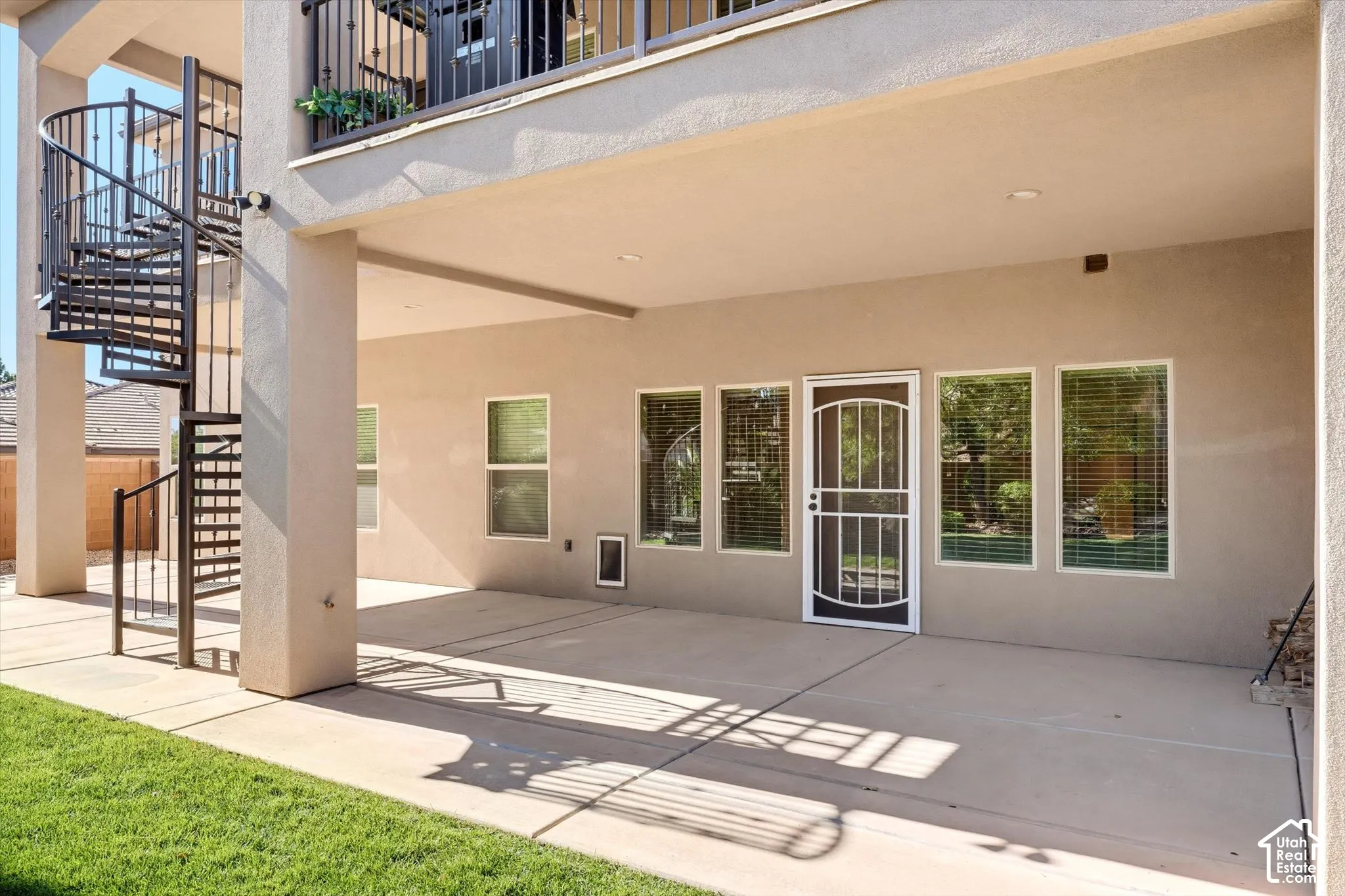 Covered patio with a concrete surface, featuring a black metal spiral staircase and a white security screen door