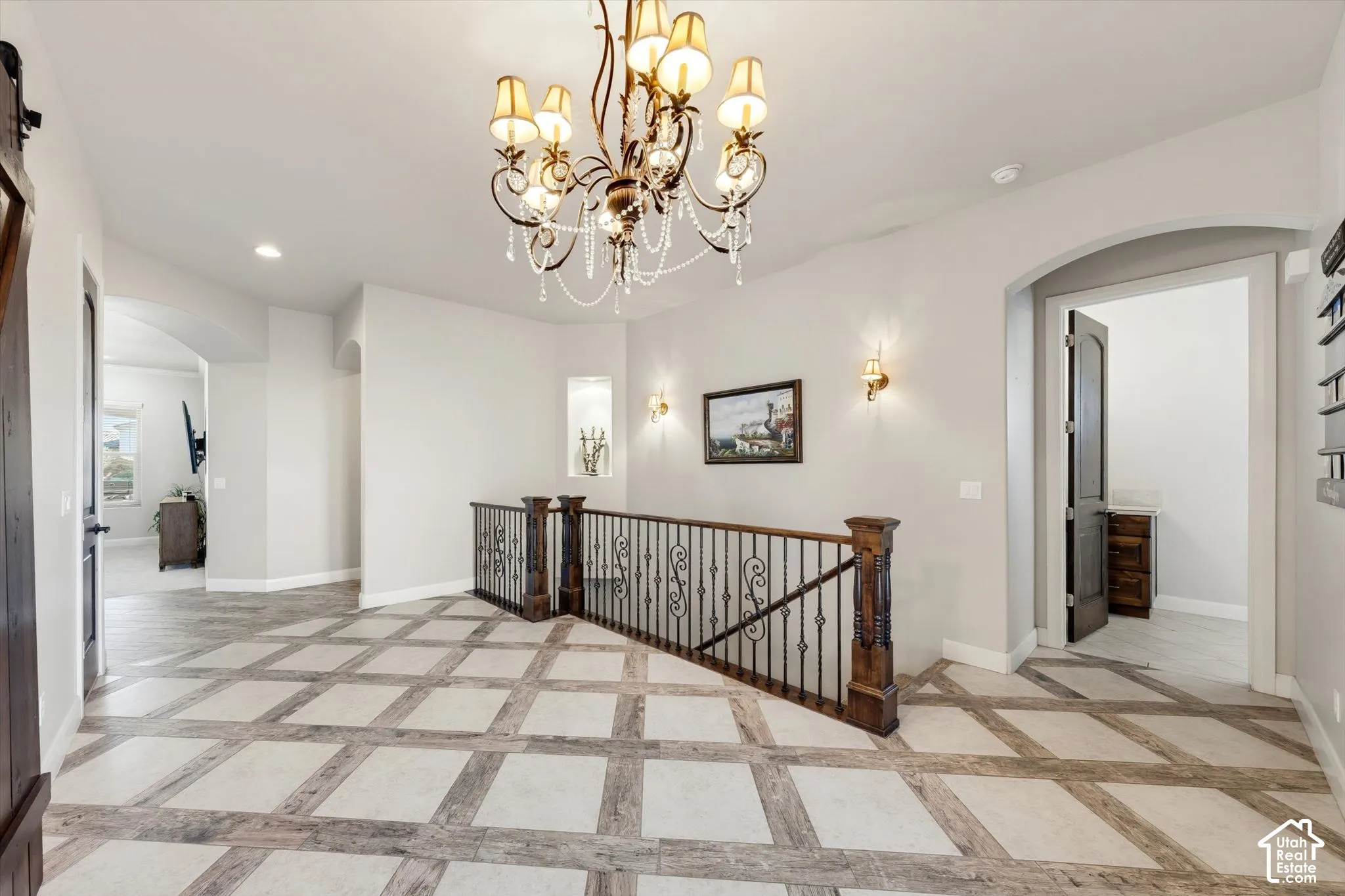 Decorative ceiling-mounted chandelier, square-pattern tile flooring, wrought iron and wood banister, recessed wall niche, and arched doorway