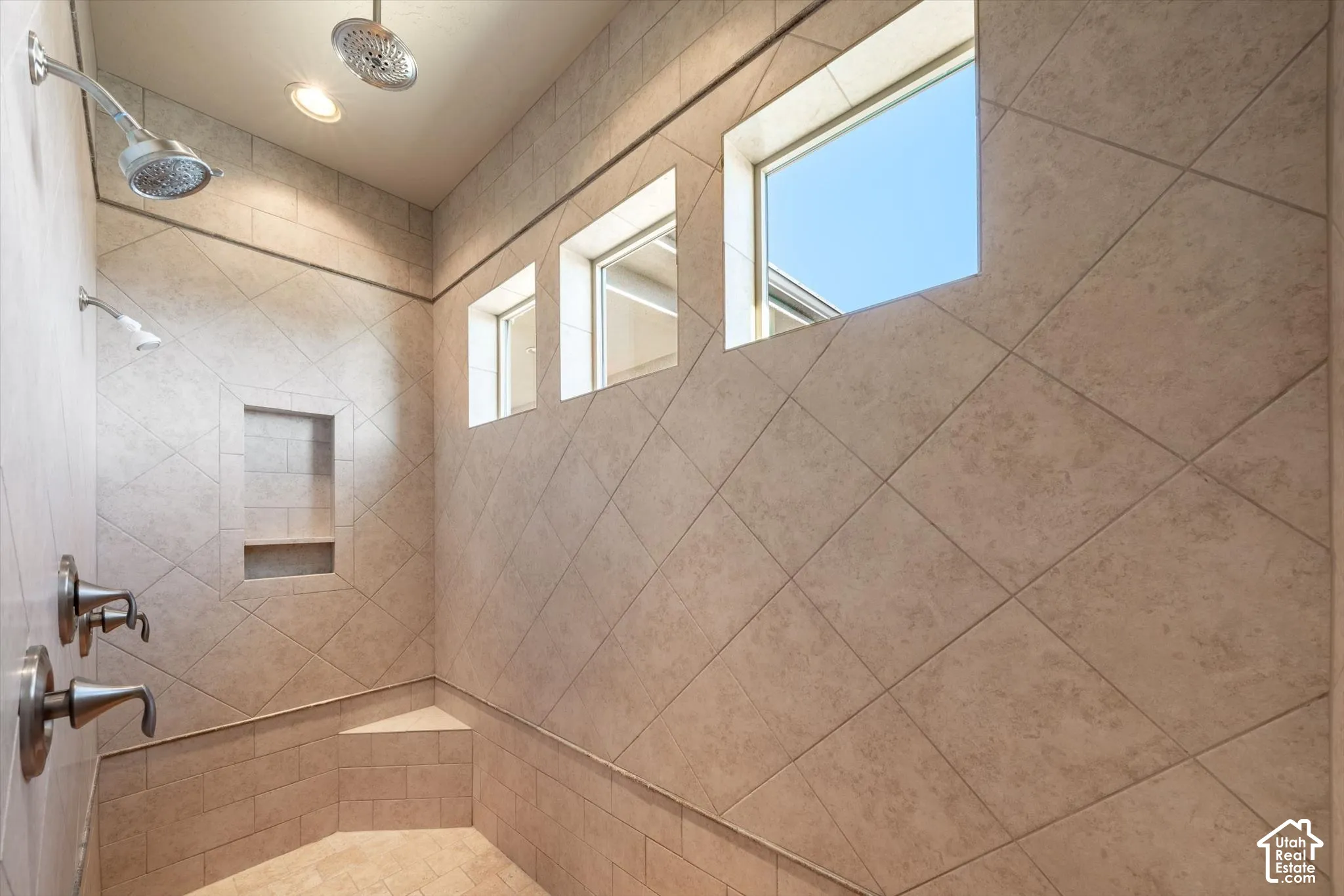 Tiled shower with a built-in bench, recessed shelf, multiple shower heads, and three clerestory windows