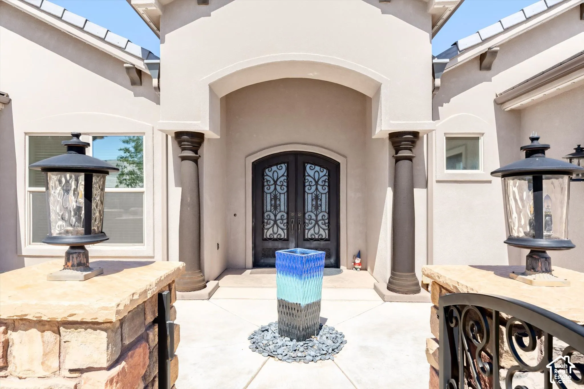 Stucco exterior with an arched entryway, decorative double entry doors, fluted columns, and exterior lighting fixtures