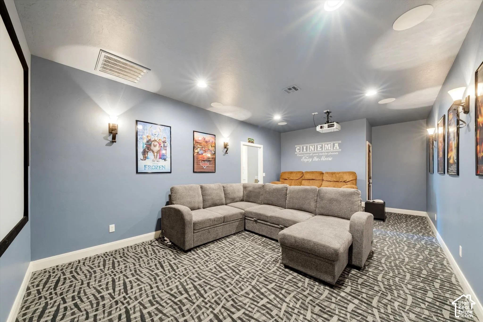 Dedicated media room featuring patterned carpeting, recessed ceiling lighting, wall-mounted sconces, and a built-in projector with screen