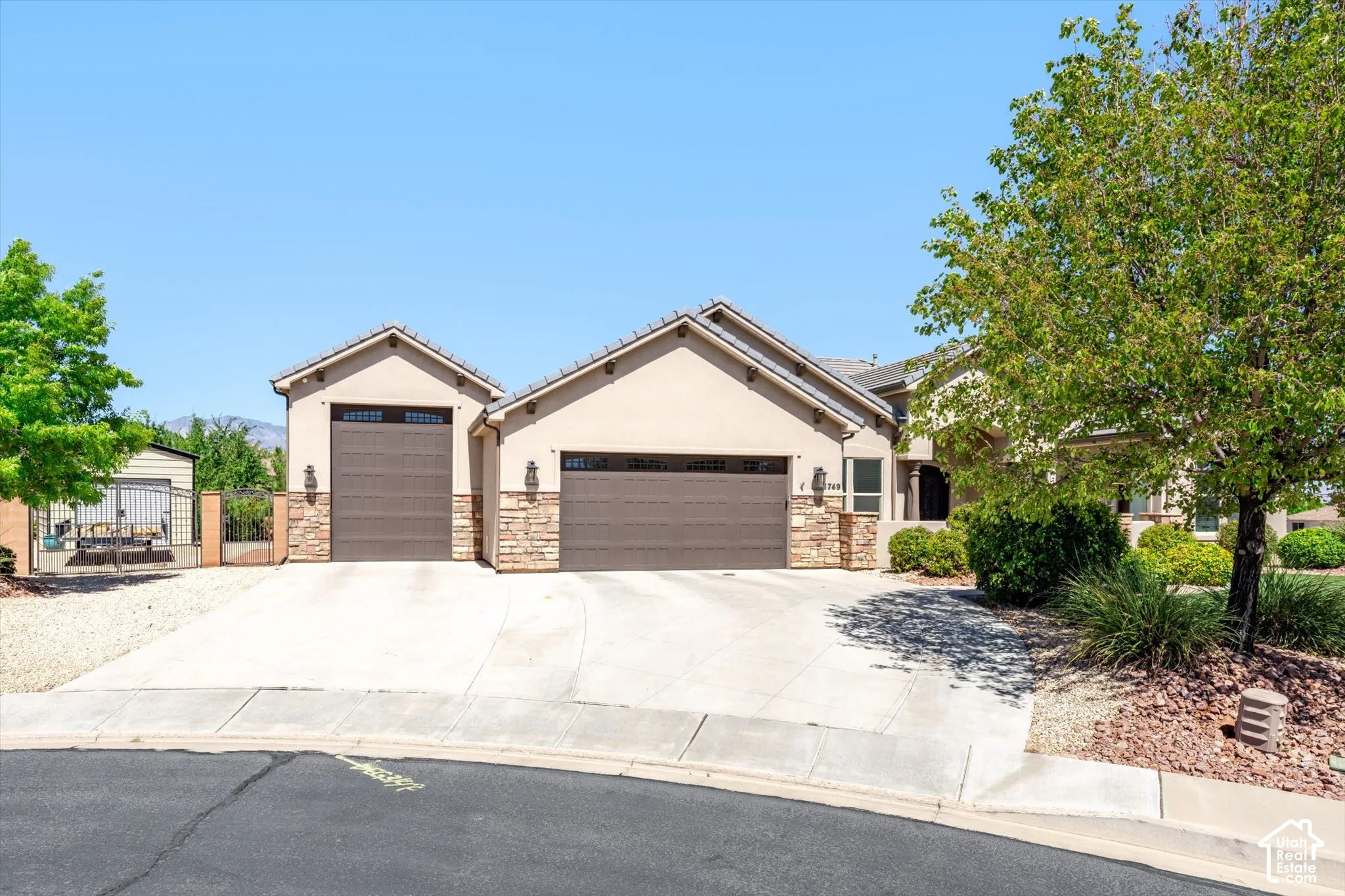 Stucco exterior with stone accents, integrated two-car garage, separate single-car garage, and mature landscaping