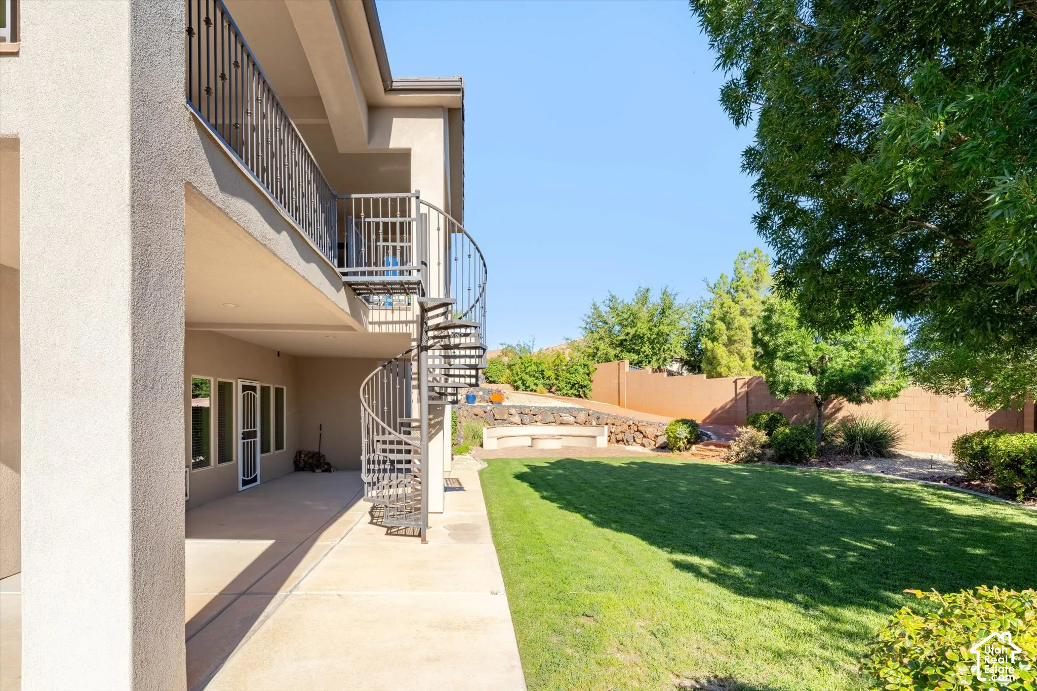 Ground-level patio with an overhead balcony, featuring a wrought iron spiral staircase