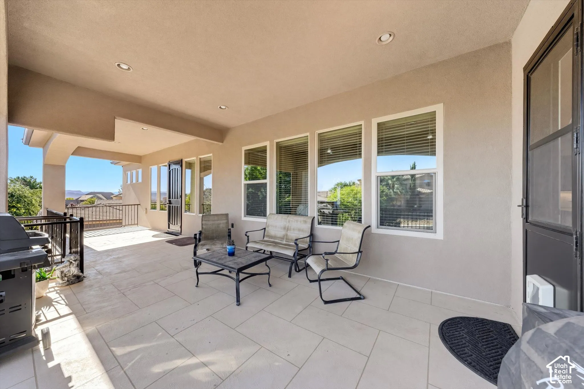 Covered outdoor patio featuring light-toned tile flooring, recessed lighting, and a black wrought iron railing