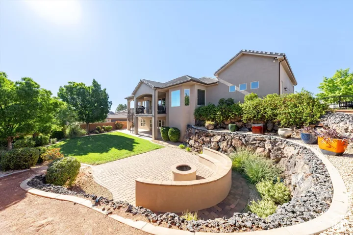 Expansive backyard featuring a manicured lawn, multi-level hardscaping, a paver patio with a built-in fire pit, and a covered balcony