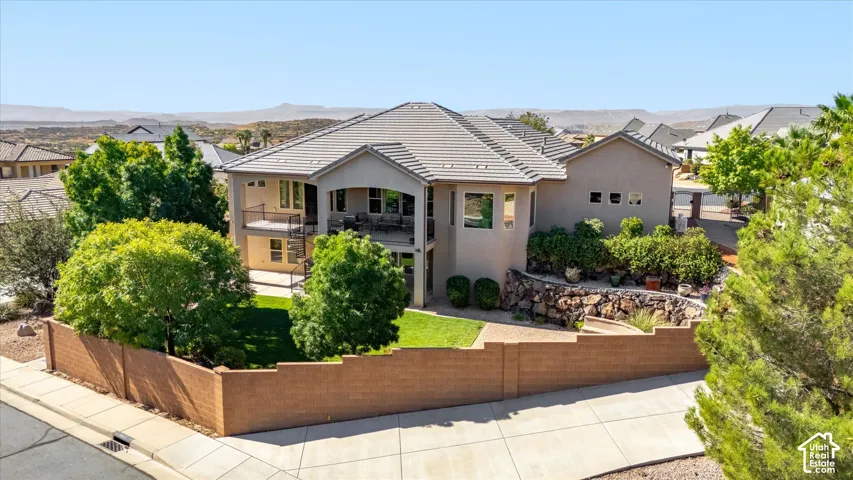 Stucco exterior residence featuring a tiled roof, upper and lower covered balconies, and a terraced rock garden
