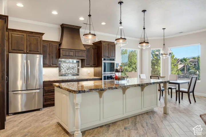 Gourmet kitchen featuring a large central island with granite countertops, rich wood cabinetry, stainless steel appliances, and wood-finish flooring