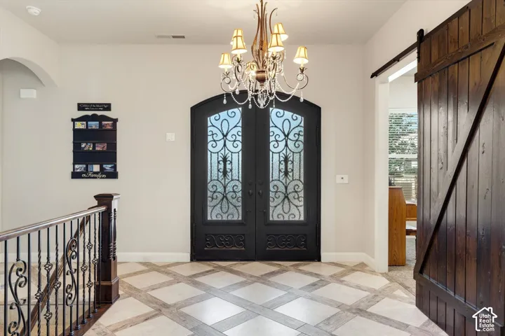Arched double entry doors with decorative ironwork, decorative chandelier, patterned tile flooring, wood and iron stair railing, and a wood barn door