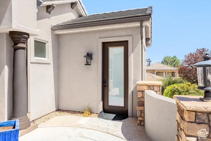 Stucco exterior with decorative corbels, full-light entry door, exterior wall lantern, stone-clad pillar, and curved stucco wall