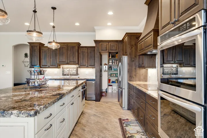Kitchen featuring an expansive island with a polished stone countertop, rich wood cabinetry, stainless steel double ovens, and recessed lighting