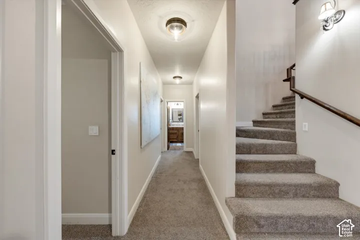 Carpeted staircase with dark wood-finish handrail, leading to a hallway with recessed lighting and a visible room with a wood-finish vanity