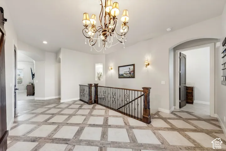 Decorative ceiling-mounted chandelier, square-pattern tile flooring, wrought iron and wood banister, recessed wall niche, and arched doorway