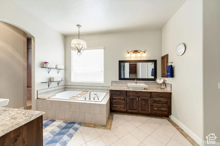 Soaking tub with tiled surround, wood-finish vanity with vessel sink, and an arched doorway