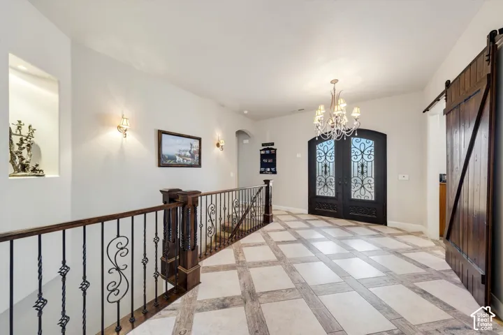 Wrought iron double entry doors with arched transom, wood-finish and tile flooring, wrought iron staircase railing with wood handrail, built-in wall niche, and decorative chandelier