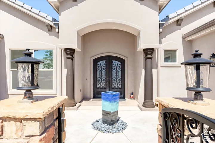 Stucco exterior with an arched entryway, decorative double entry doors, fluted columns, and exterior lighting fixtures