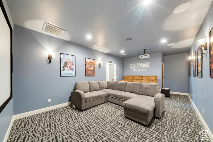 Dedicated media room featuring patterned carpeting, recessed ceiling lighting, wall-mounted sconces, and a built-in projector with screen