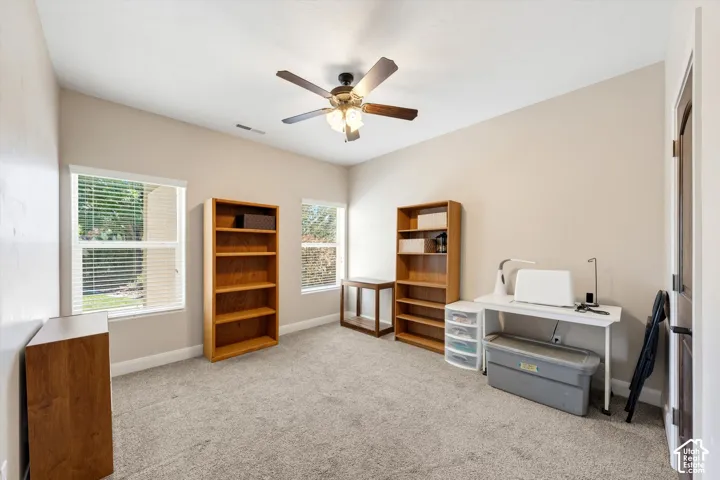 Carpeted room with a ceiling fan, two windows, and a dark wood-finish door