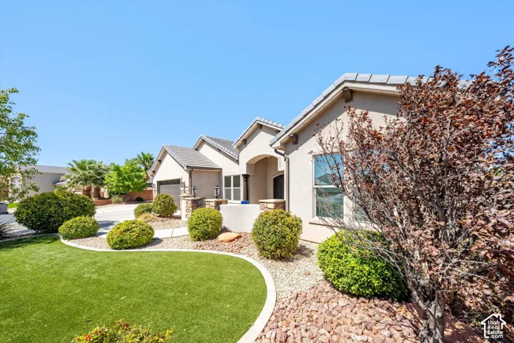 Stucco exterior with a tiled roof, featuring a paved driveway, and landscaping with artificial turf and decorative rock