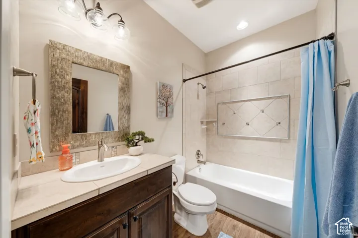 Bathroom featuring a vanity with an undermount sink, a framed mirror, a three-light fixture, a toilet, and a bathtub with tiled surround