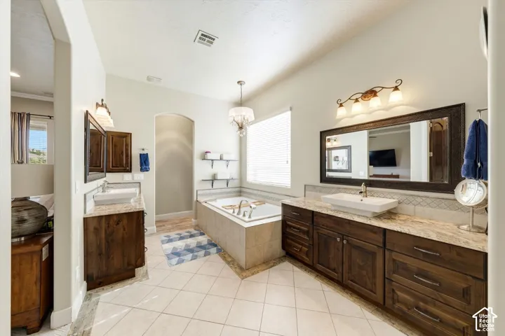Spacious bathroom featuring a built-in soaking tub, dual vanity with vessel sinks, tile flooring, and warm wood-finish cabinetry