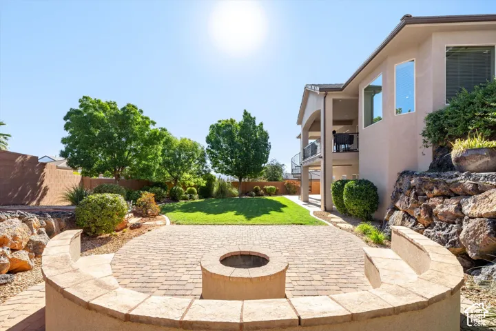 Paver patio with a built-in fire pit and curved seating wall, stucco exterior, raised rock landscaping, and a manicured lawn