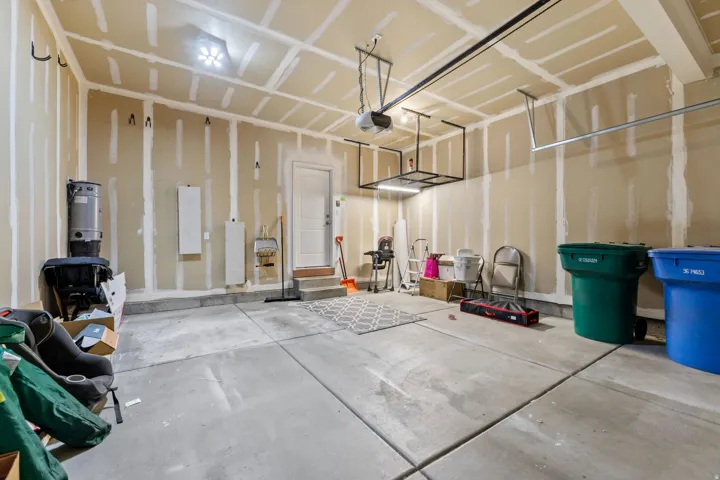Attached garage with exposed wall framing, concrete flooring, and an overhead storage rack
