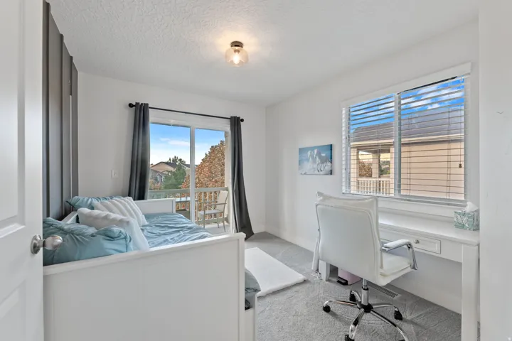 White walls with ceiling-mounted light fixture, sliding glass door with balcony, window with horizontal blinds, and a built-in desk