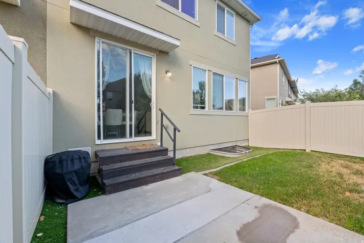 Private fenced yard with concrete patio, steps to sliding glass door, and a ground-level window well