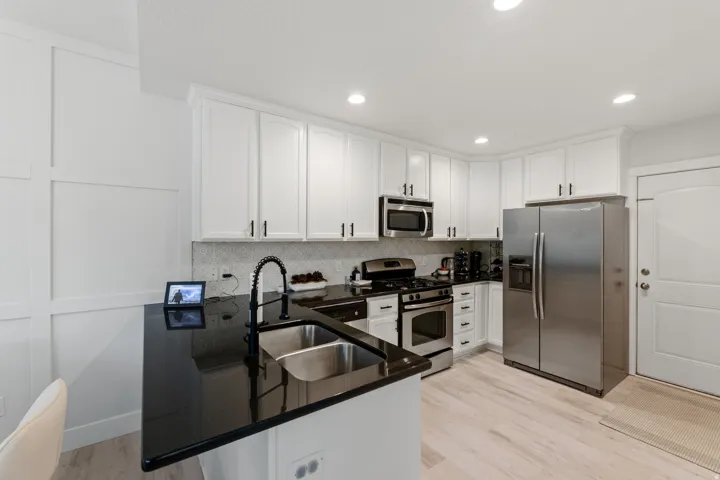 White shaker cabinetry, dark countertops, stainless steel appliances, modern backsplash, and wood-finish flooring
