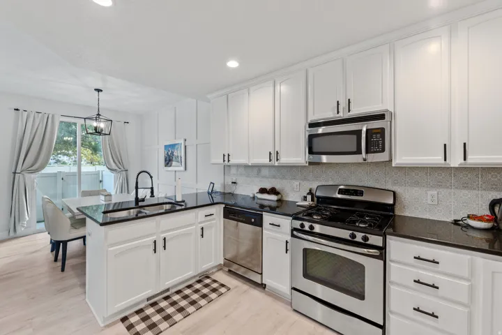 Kitchen featuring white cabinetry, black countertops, stainless steel appliances, and wood-finish flooring