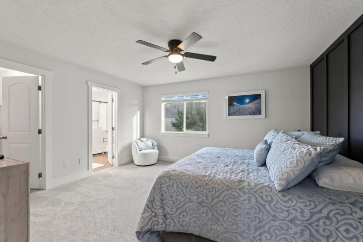 Spacious room featuring light-toned carpeting, a ceiling fan, a window, and a built-in dark panel accent wall