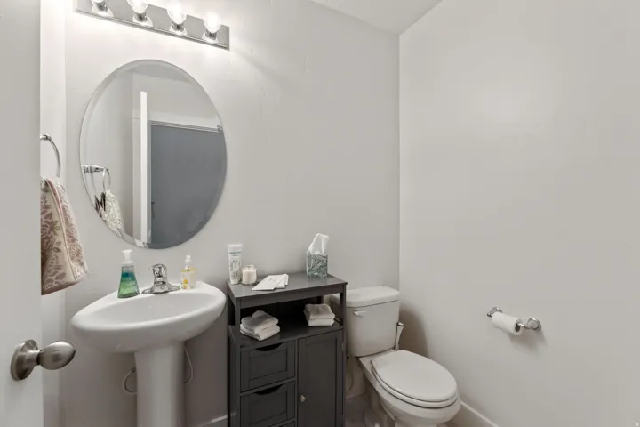 Contemporary bathroom featuring a circular framed mirror with integrated lighting, pedestal sink, black cabinetry with open shelving, ceramic tile flooring, and chrome hardware throughout